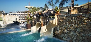 A pool with a waterfall feature, lounge chairs, and a stone wall. - Alba Seleqtta (Lloret de Mar)