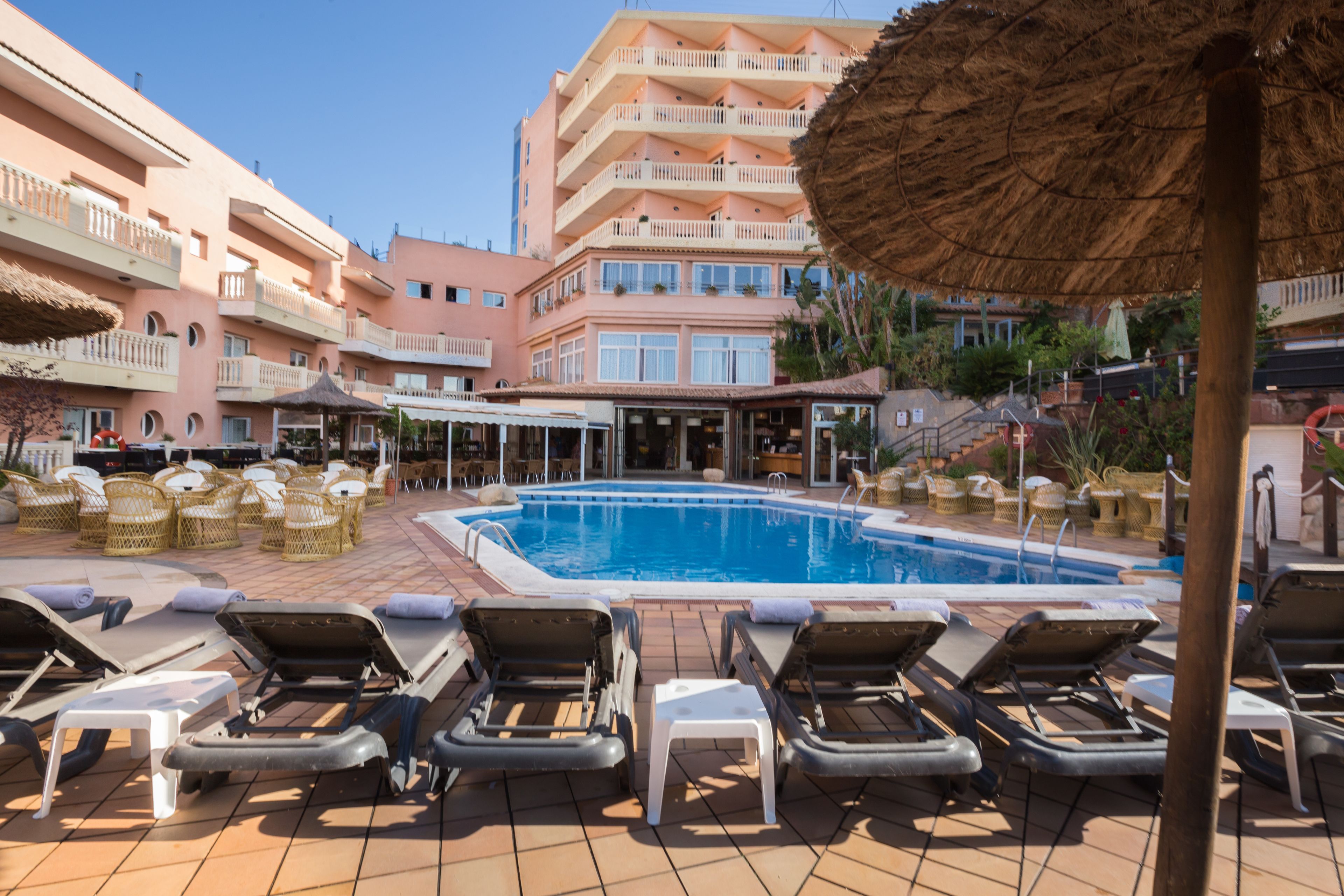 Et hotelområde med swimmingpool, liggestole og en bygning med altaner.
