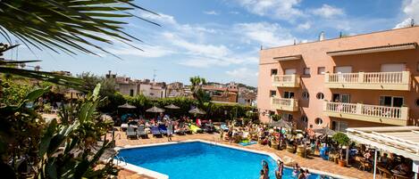 A swimming pool surrounded by lounge chairs and umbrellas, with a building in the background.