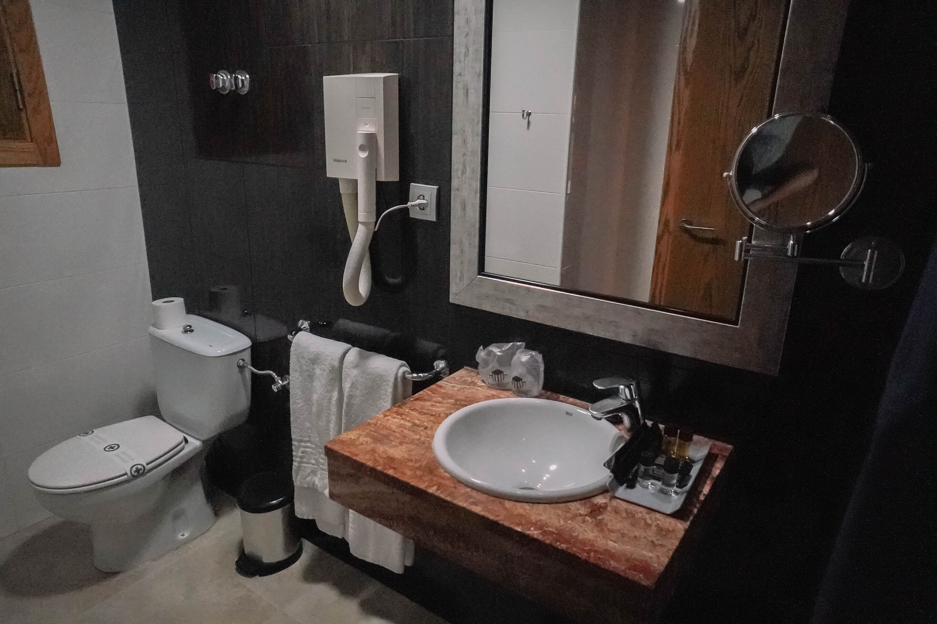 A bathroom with a toilet, sink, mirror, and towel rack.