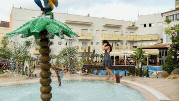 A fountain with a green top and a bird sculpture, surrounded by a pool and a building with balconies.