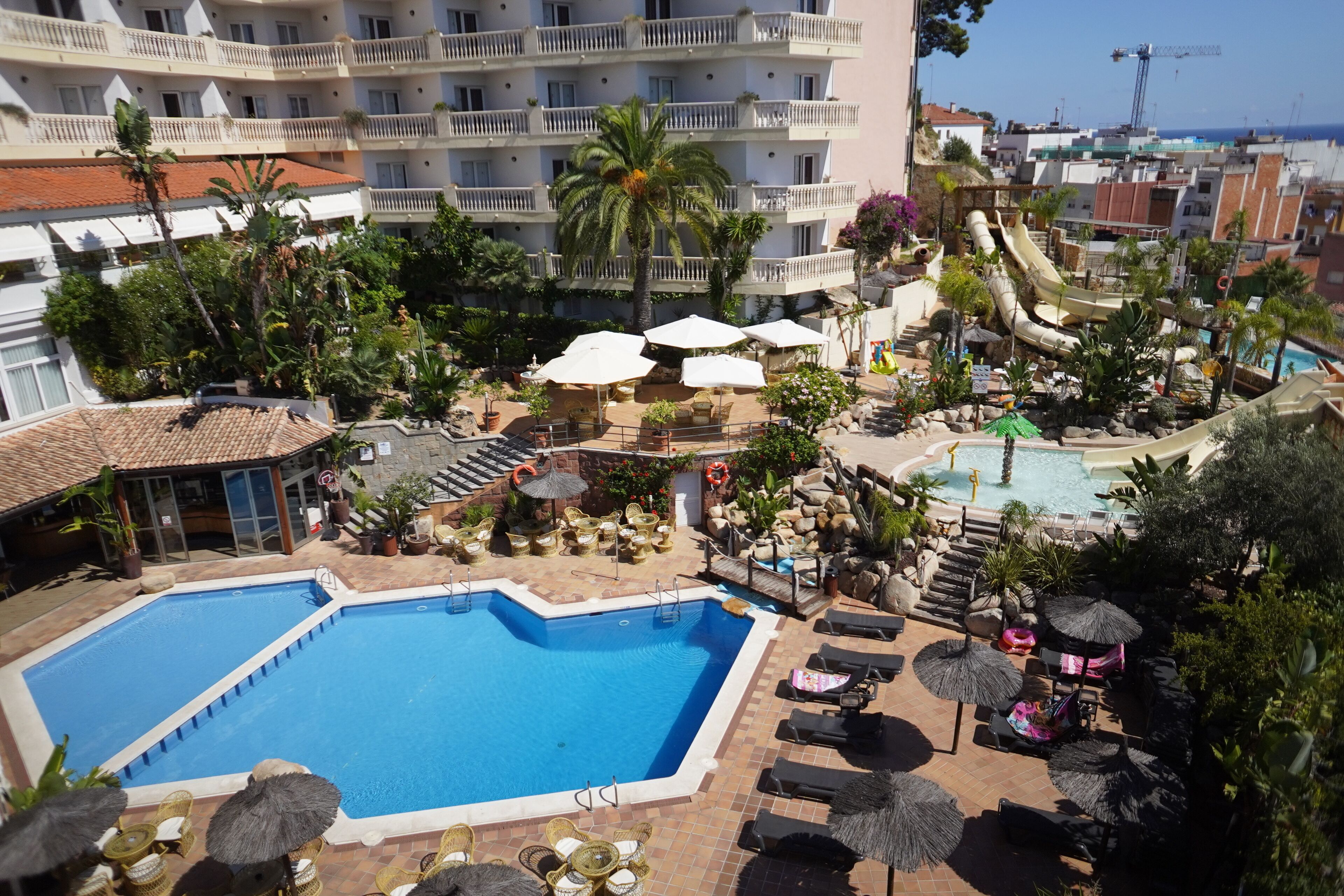 Een zwembadgedeelte van een hotel met meerdere zwembaden, ligbedden, parasols en een waterglijbaan.