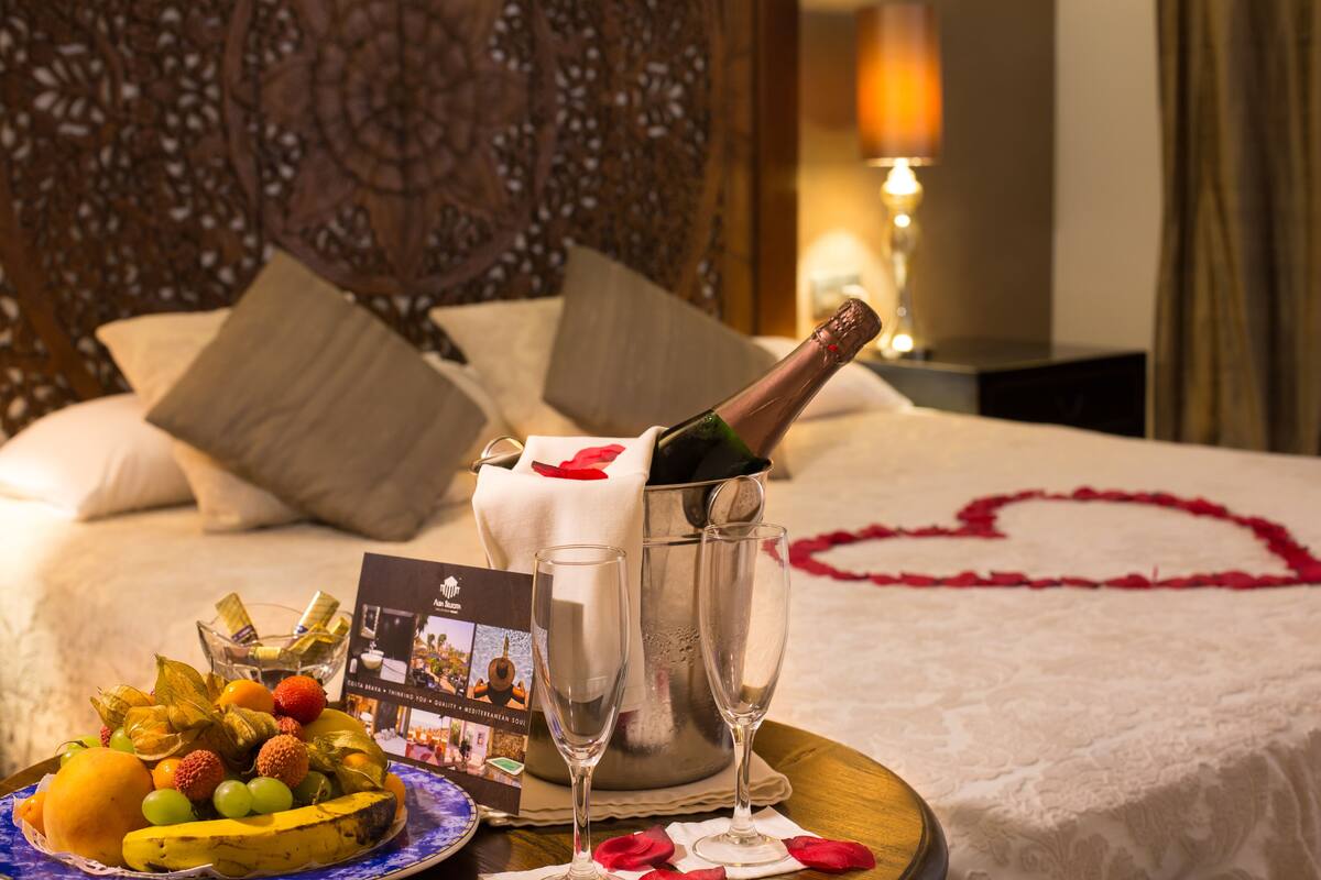 A bed with a heart-shaped decoration, a bottle of champagne, and a fruit platter.