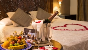 Una cama con una decoración con forma de corazón, una botella de champán y una bandeja de frutas.