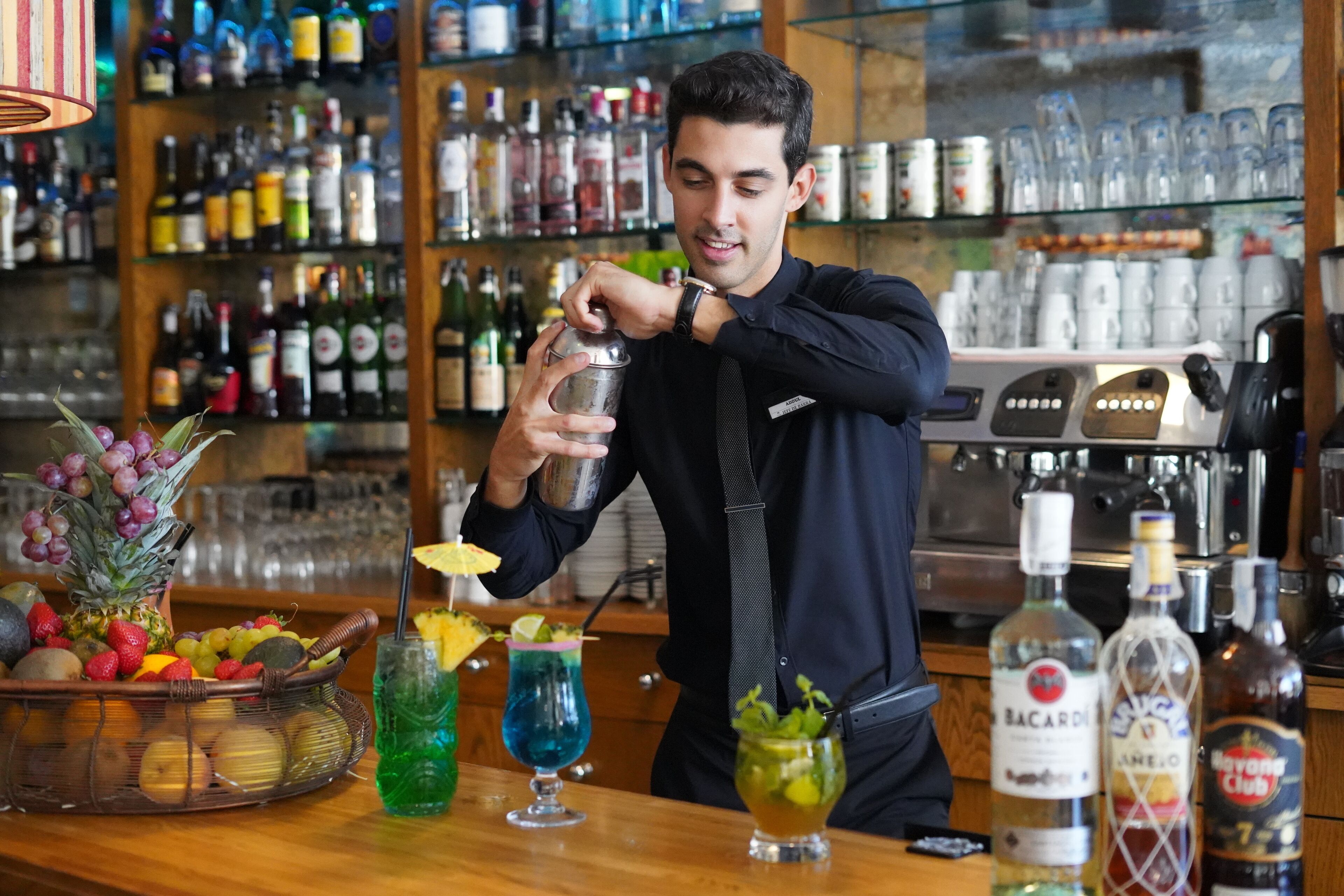 A bartender preparing a drink at a bar with a variety of bottles and glasses in the background.