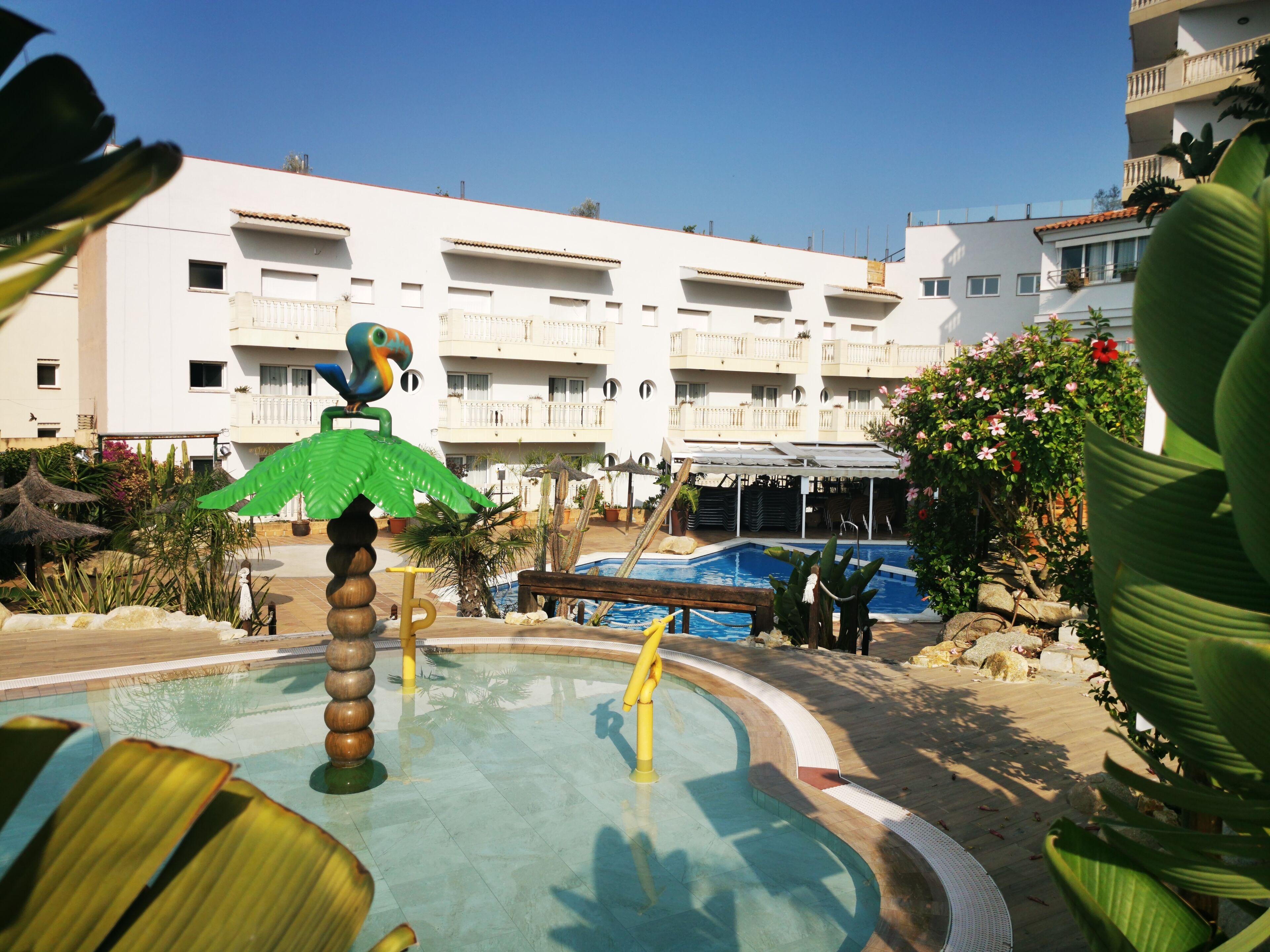 A pool area with a water slide, palm trees, and a building with balconies in the background.