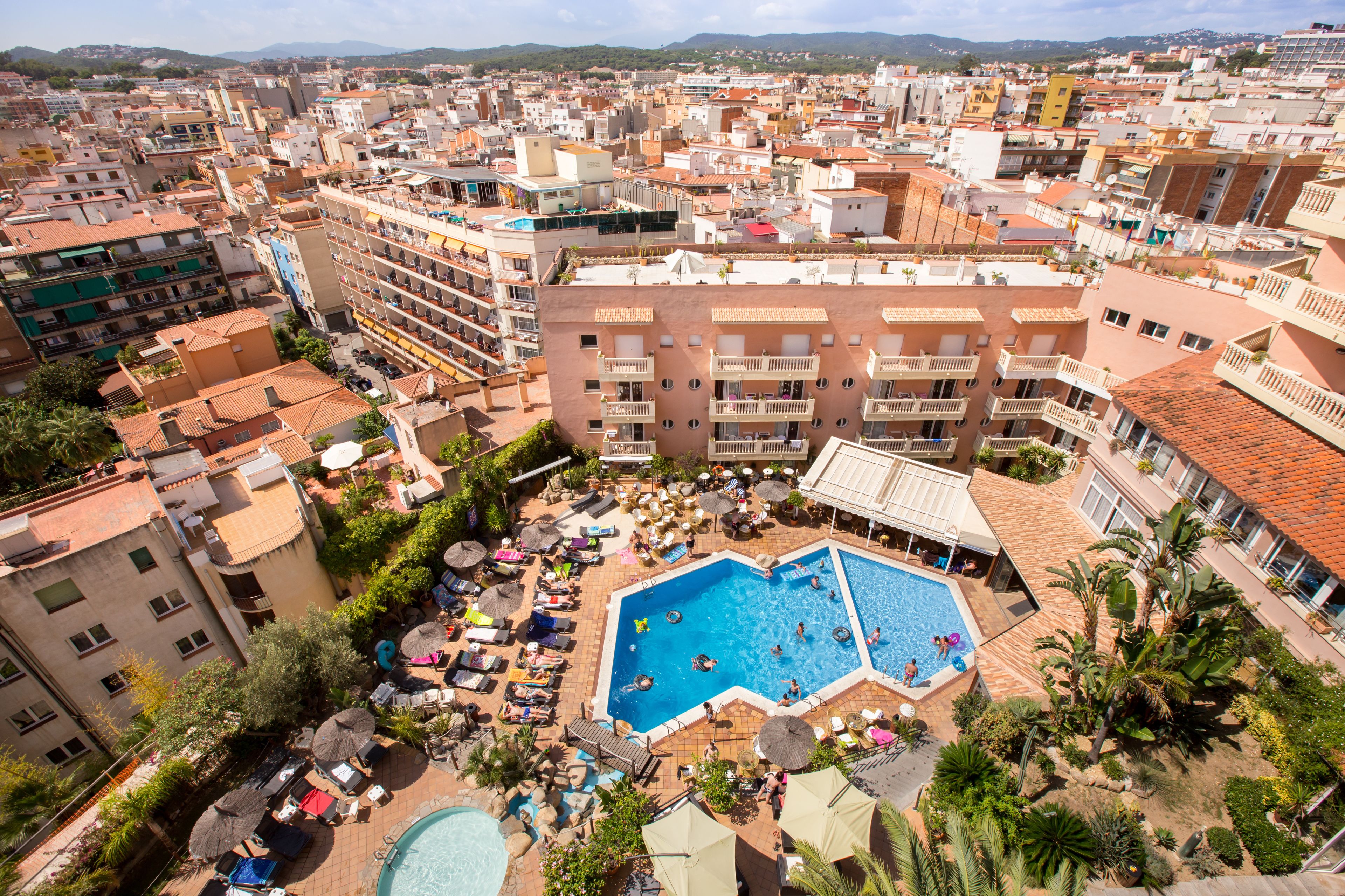 Un hotel con piscina en la azotea, rodeado de sillones de descanso y sombrillas, ubicado en una zona urbana densamente construida.