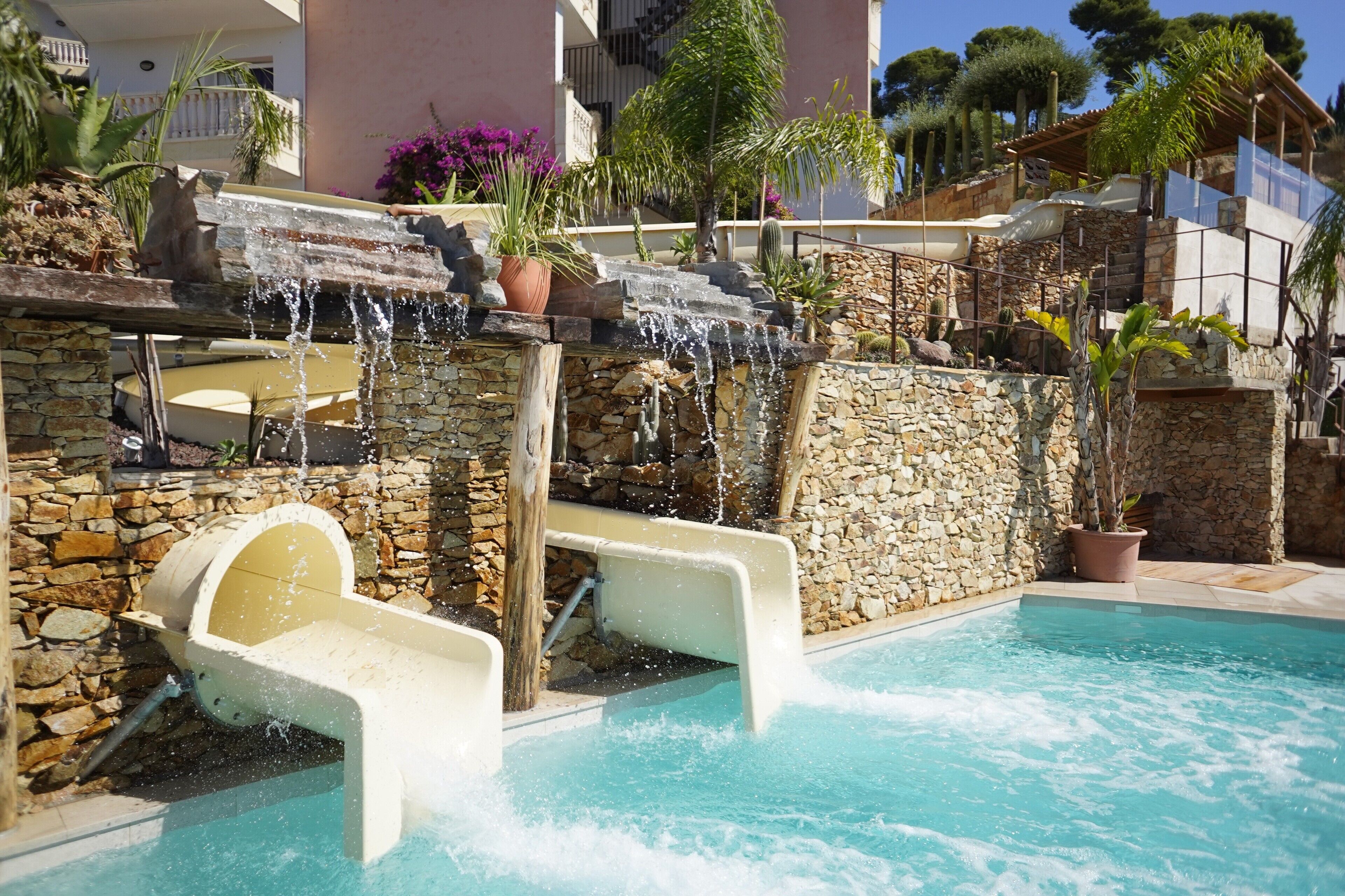 Una piscina con cascada, paredes de piedra y plantas en macetas.