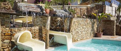 Una piscina con cascada, paredes de piedra y plantas en macetas.