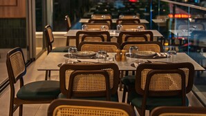 An outdoor dining area with tables set for two, wicker chairs, and a hanging light fixture.