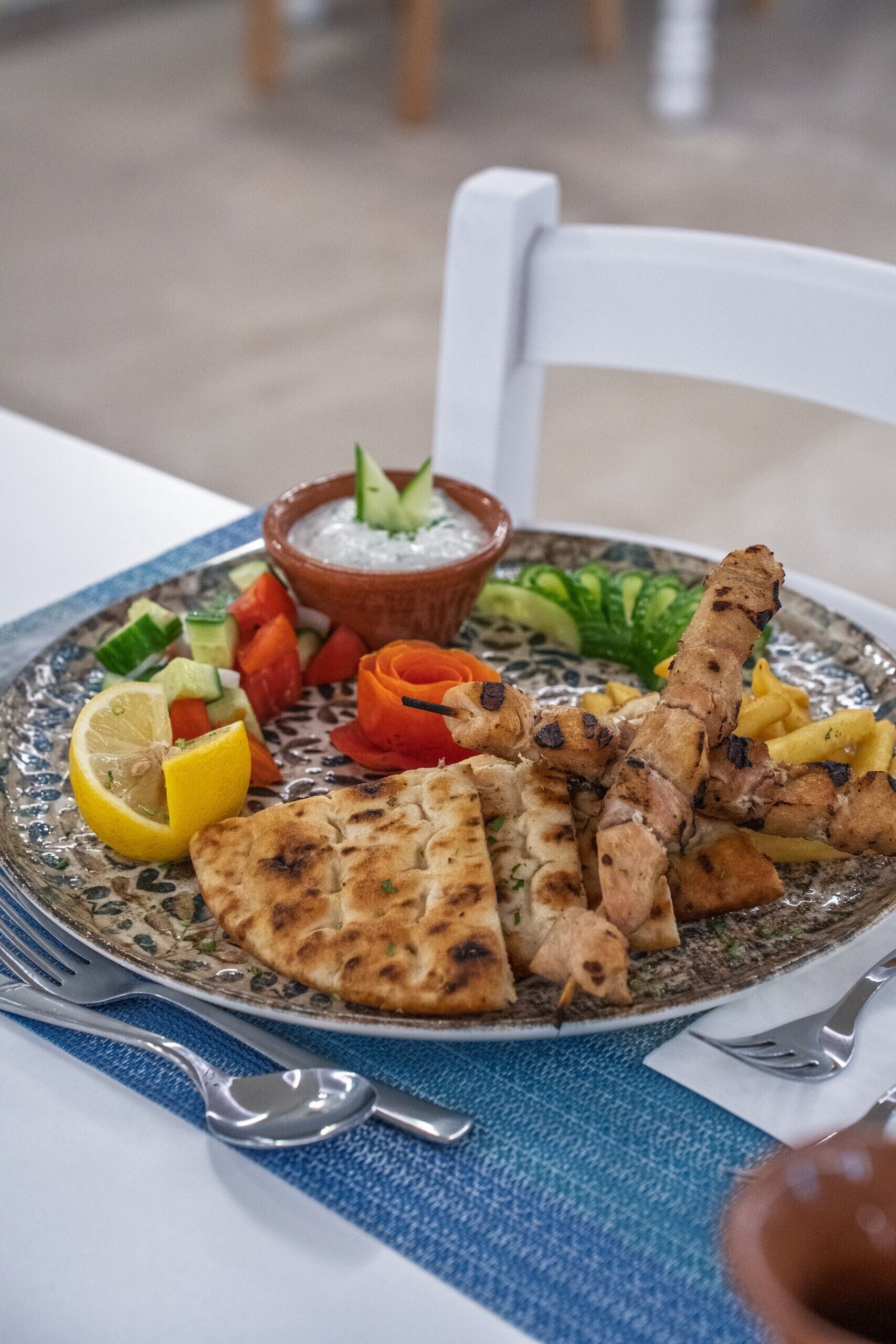 Un plato de comida con carne a la parrilla, verduras y un recipiente con salsa.