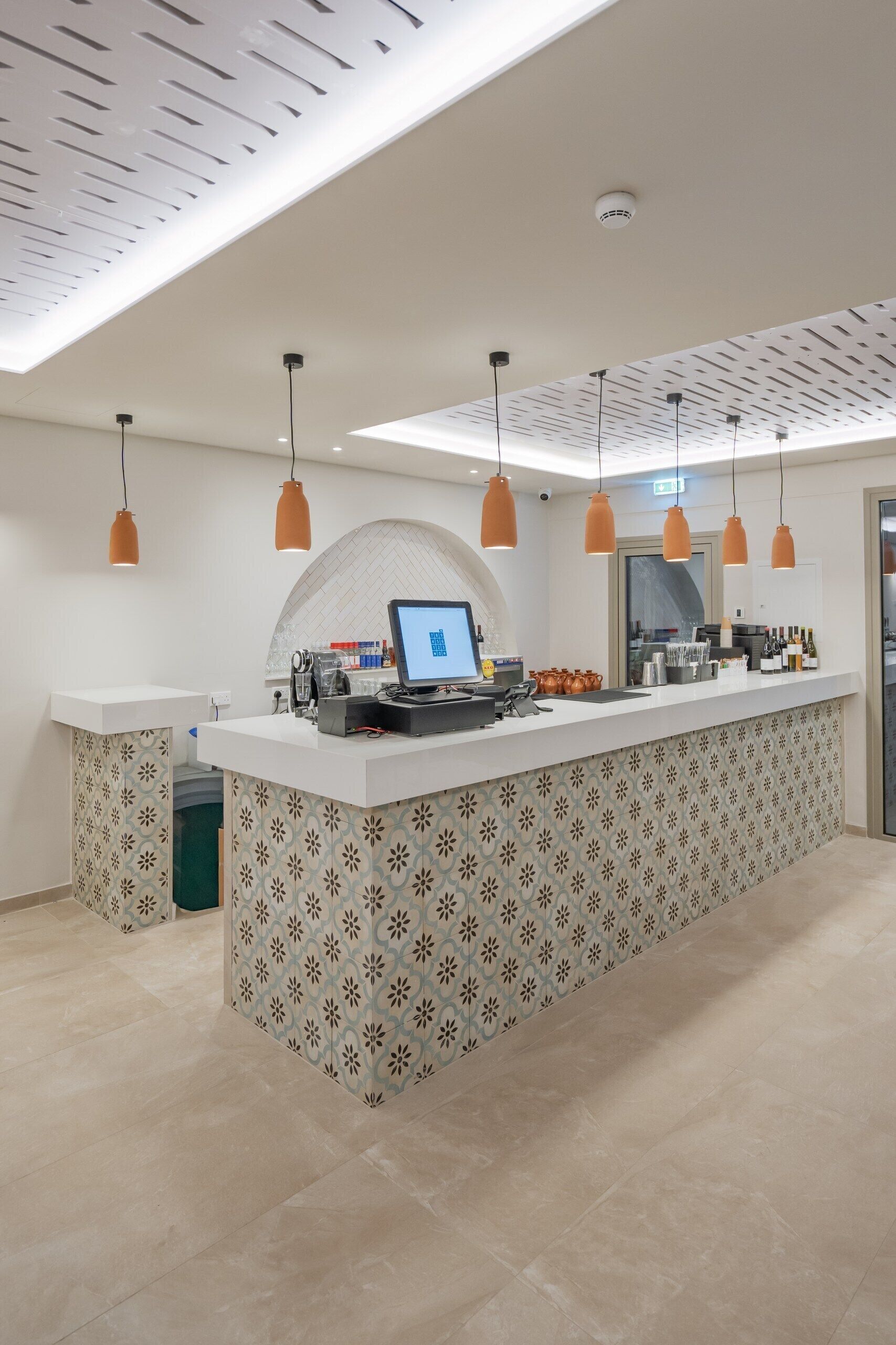 Zona bar moderna con un bancone centrale, illuminazione a sospensione e uno schienale decorato.