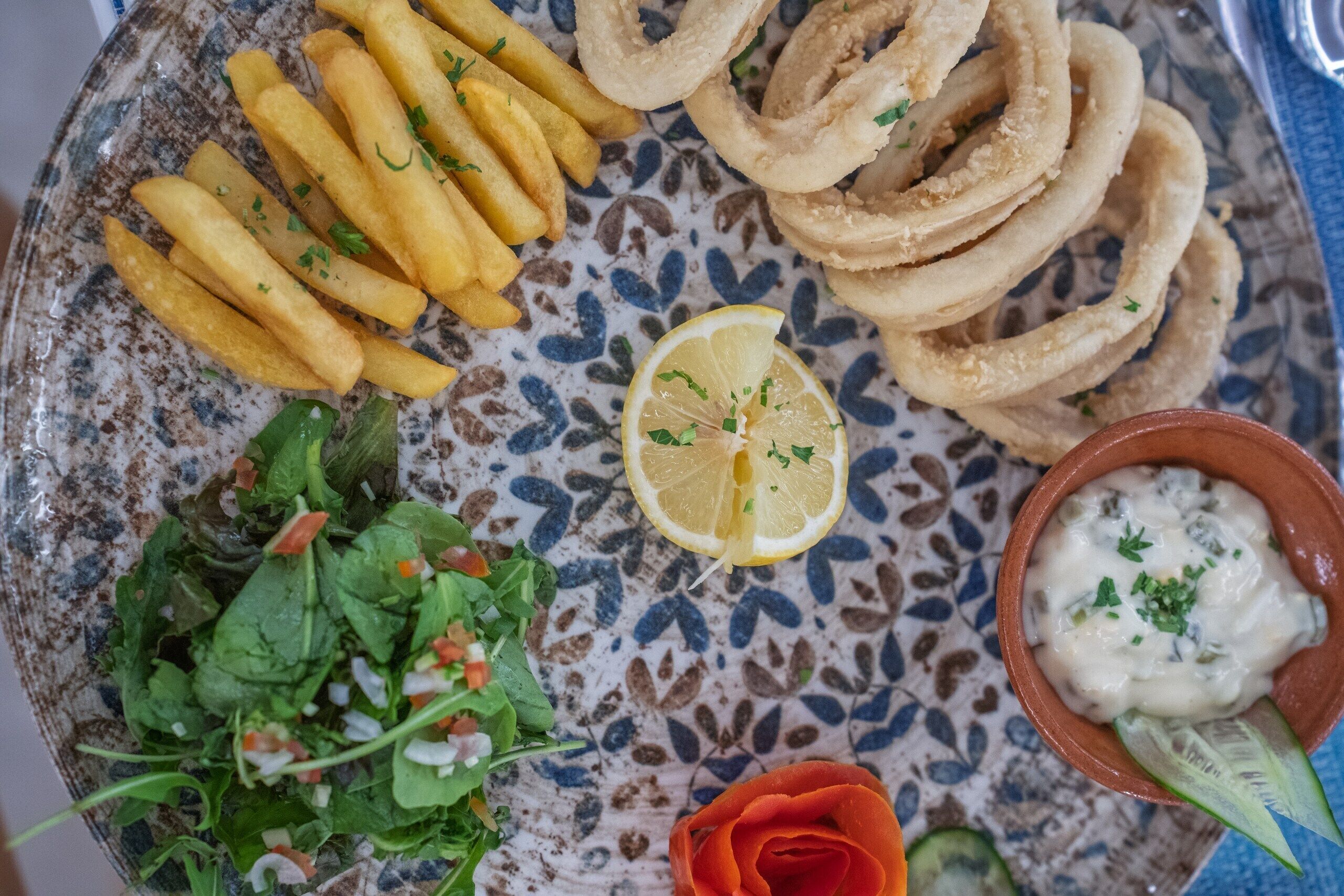 Une assiette contenant des aliments frits, une tranche de citron et un bol de sauce pour tremper.