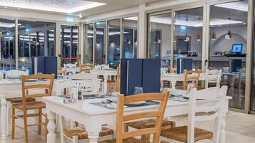 Un comedor moderno con mesas y sillas blancas, divisiones de vidrio y un techo con diseño perforado.