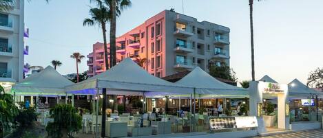 Ein Restaurant direkt am Strand mit Außenbestuhlung, Palmen und einem Gebäude mit Balkonen im Hintergrund.