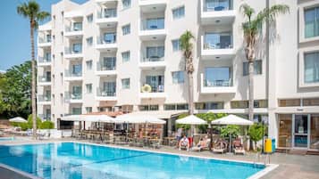 A hotel with a swimming pool, outdoor seating, and palm trees.