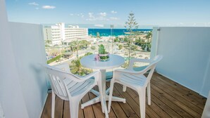 Un balcón con una mesa redonda y dos sillas blancas, con vista a una zona turística con edificios y una playa.
