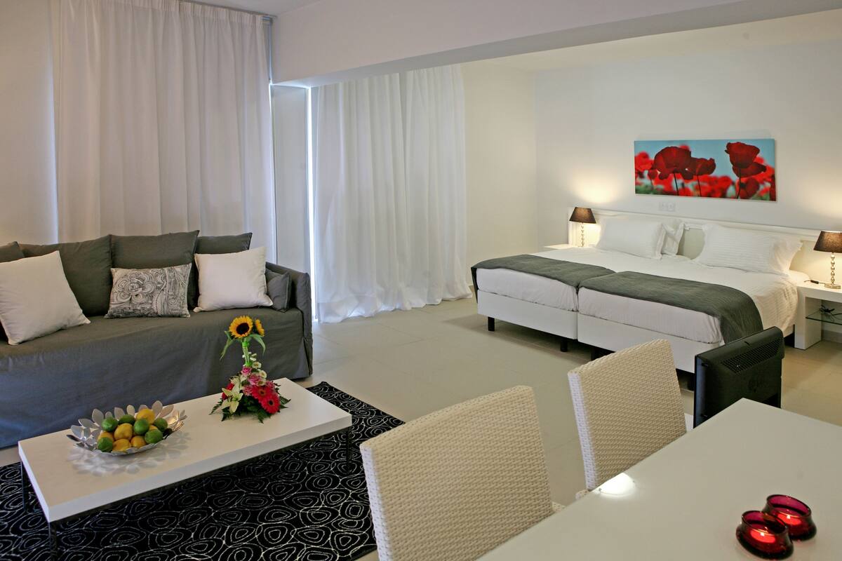 A hotel room with a bed, a sofa, a dining table, and a coffee table.