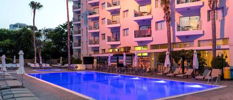 A hotel with a swimming pool, multiple balconies, and outdoor seating areas.