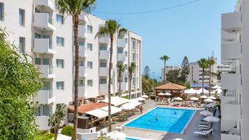 A hotel with a swimming pool surrounded by palm trees and sun loungers.