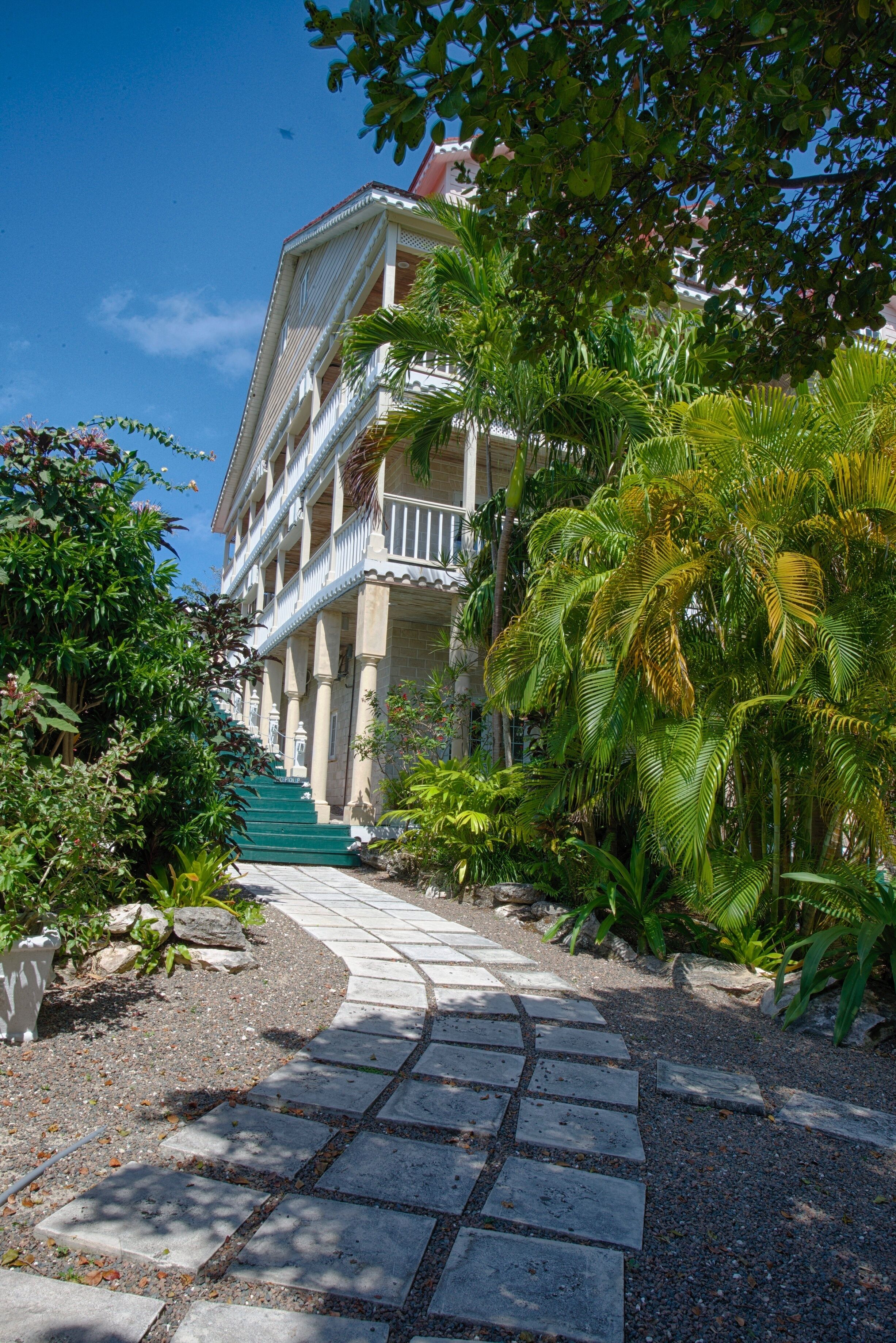 A building with a central staircase, surrounded by lush greenery and a stone pathway.