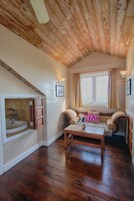 Un cuarto acogedor con techo de madera, un banco con cojines, una ventana con cortinas y una pequeña mesa con un jarrón de flores.