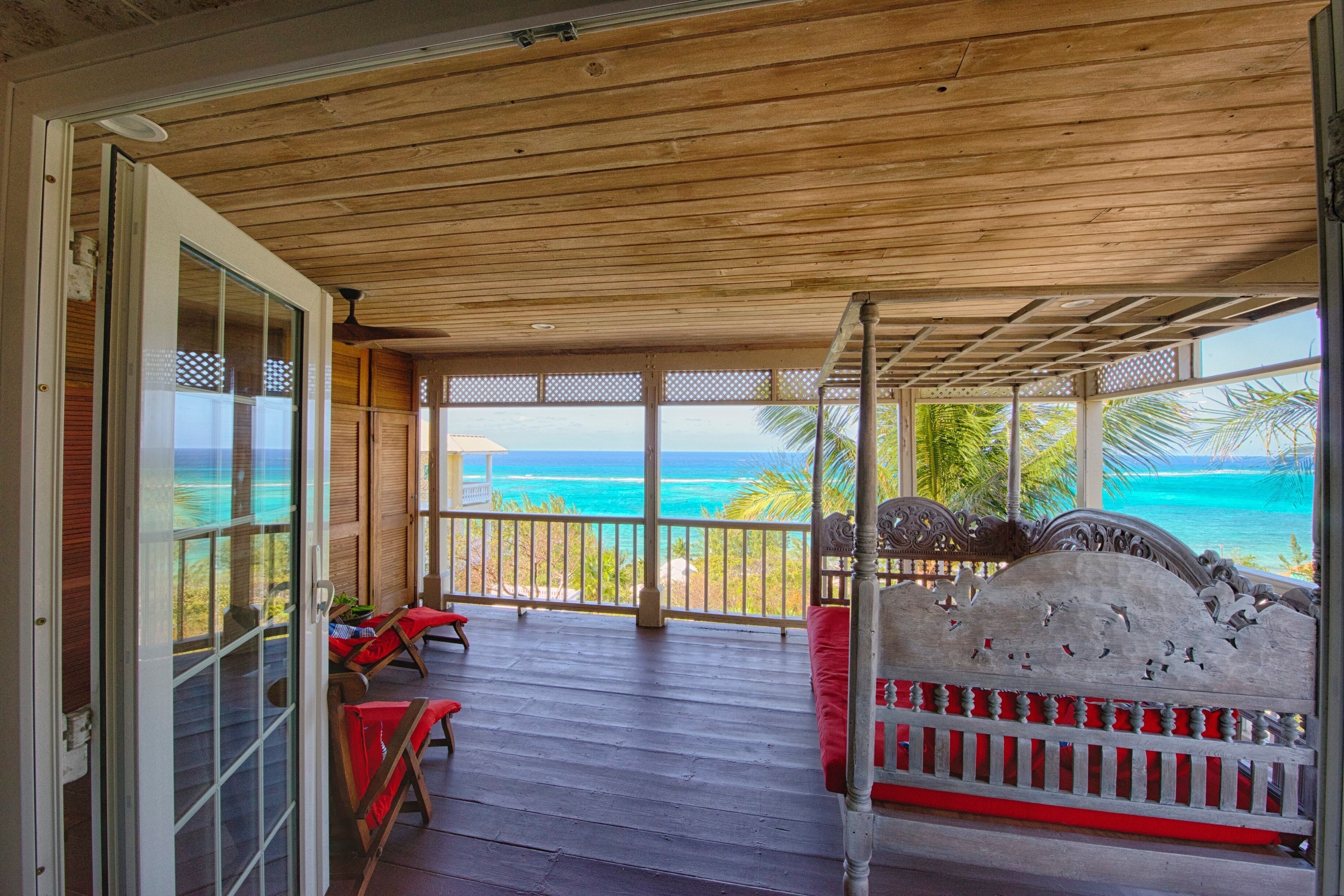 Una terraza de madera con una cama y sillas, con vista a la playa.