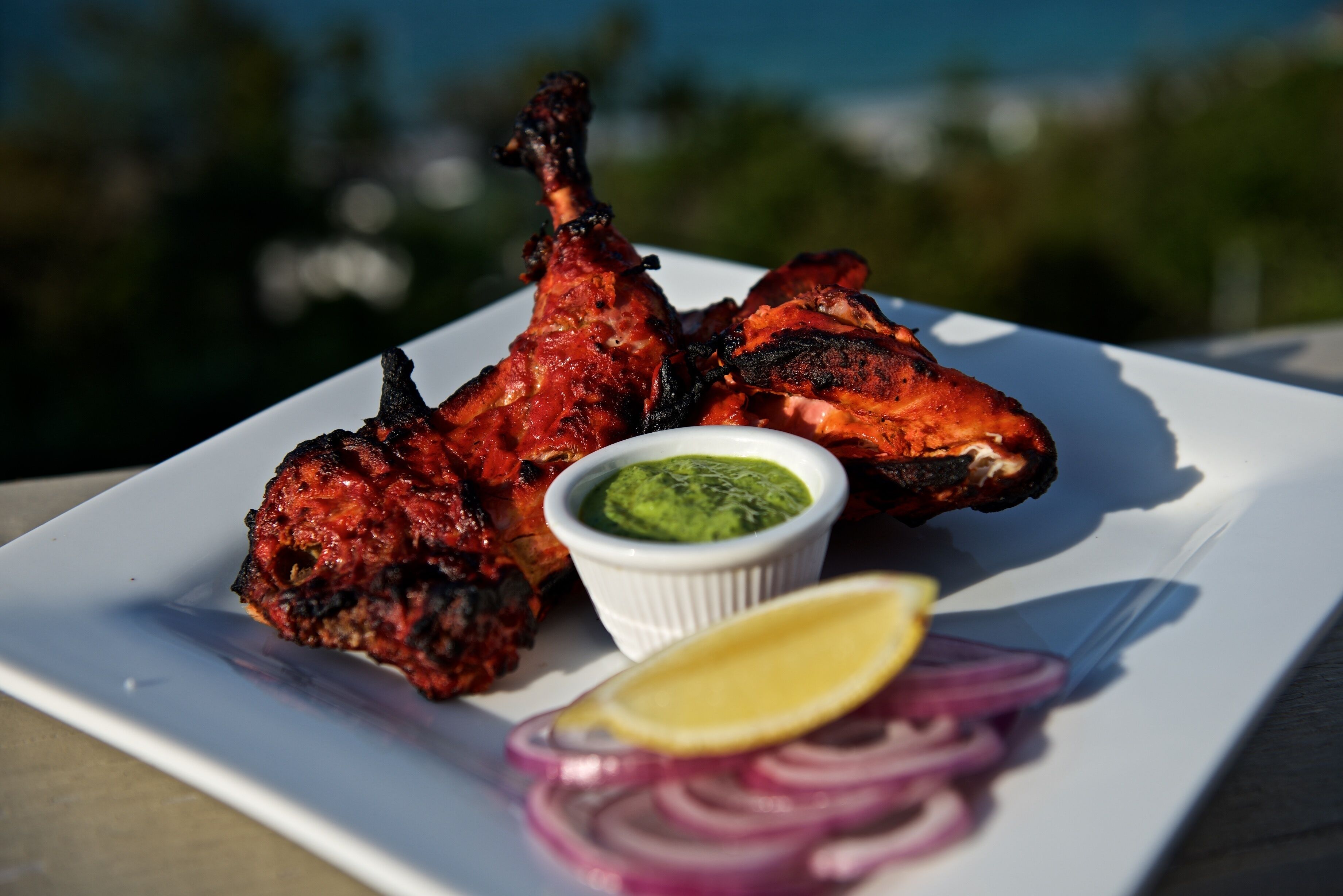 Ein Teller mit Tandoori-Hähnchen, dazu grünes Chutney und geschnittene Zwiebeln.