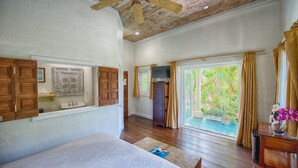 Un dormitorio con cama, ventilador de techo de madera, armario de madera y ventana con cortinas.