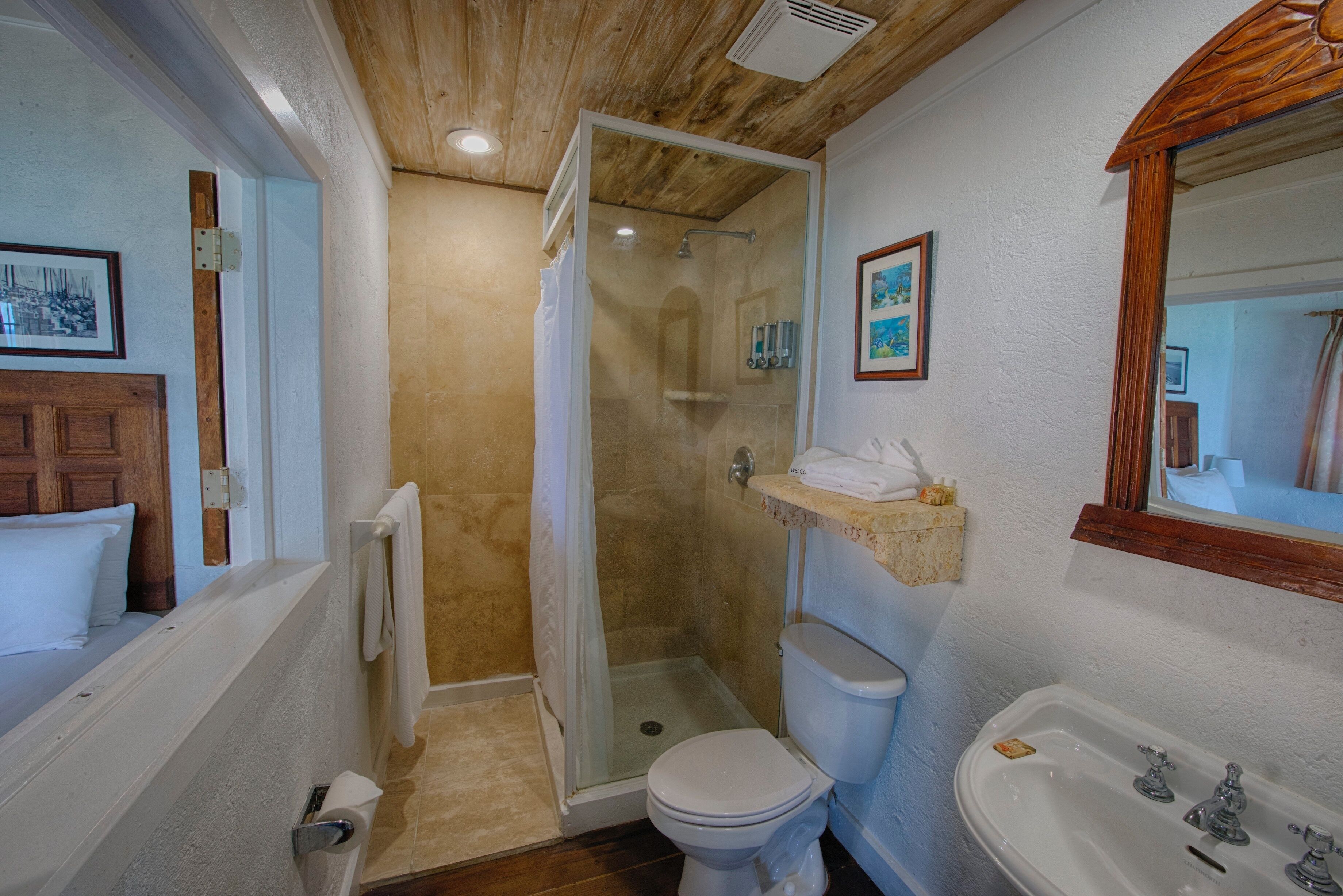 A bathroom with a shower, toilet, sink, and wooden ceiling.