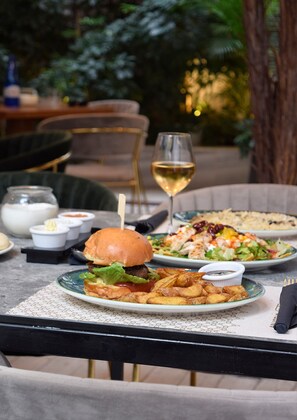 A dining table with various dishes, including a burger, salad, and fried potatoes, along with a glass of white wine. - John's Hotel (Chalcis)