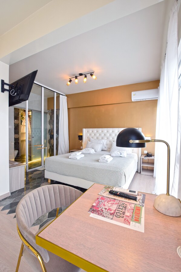 A hotel room with a bed, a desk, a chair, a TV, and a shower area. - John's Hotel (Chalcis)