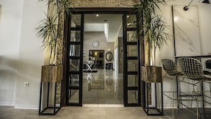 A hotel entrance with a modern design, featuring a glass door, a clock, and a seating area with chairs and a table. - John's Hotel (Chalcis)