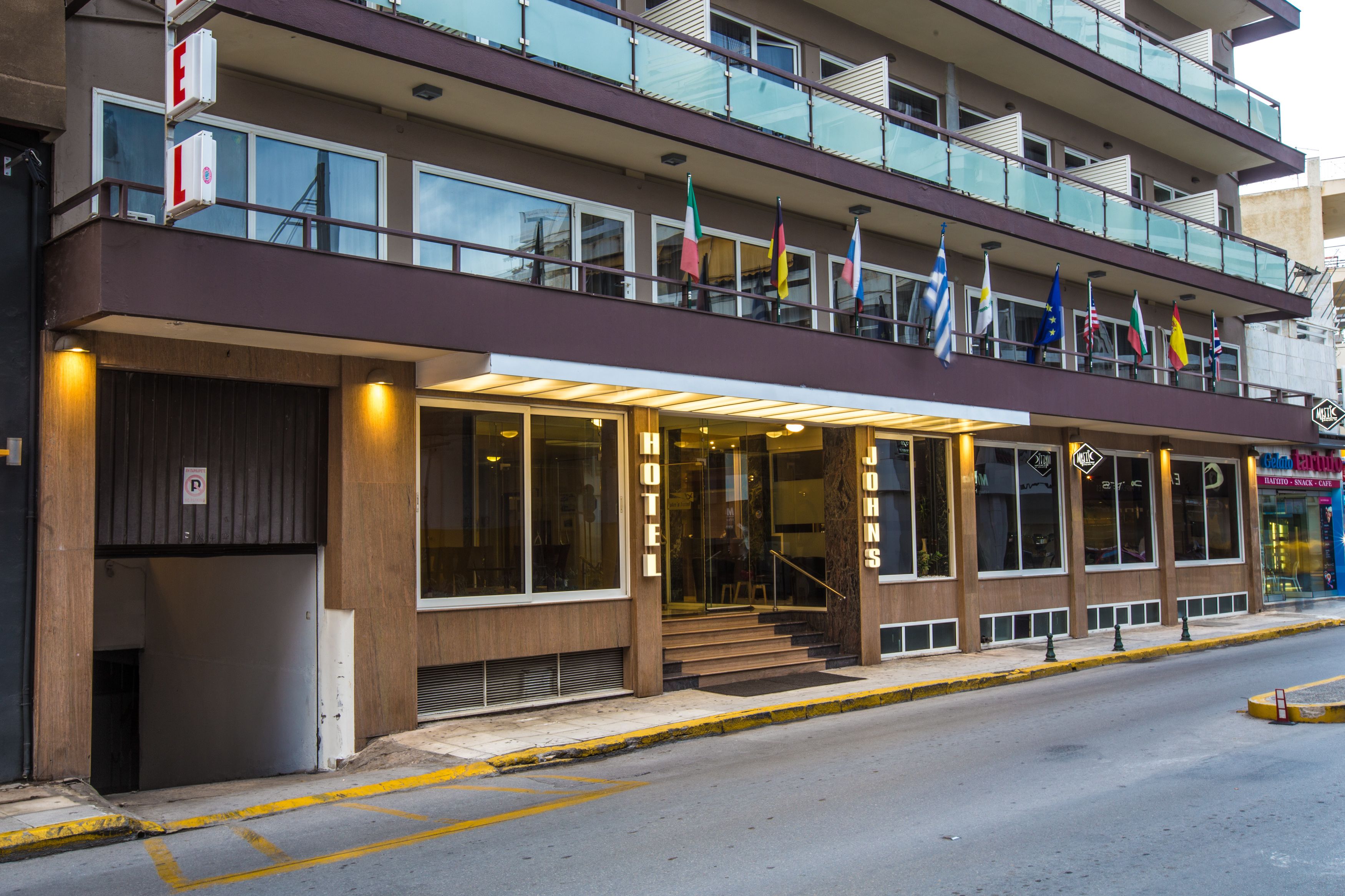 A hotel with a two-story structure, a ground-level entrance with a glass facade, and multiple flags displayed outside.