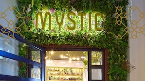 A hotel entrance with a 'MYSTIC' sign, a glass door, and a bar area visible through the doorway. - John's Hotel (Chalcis)