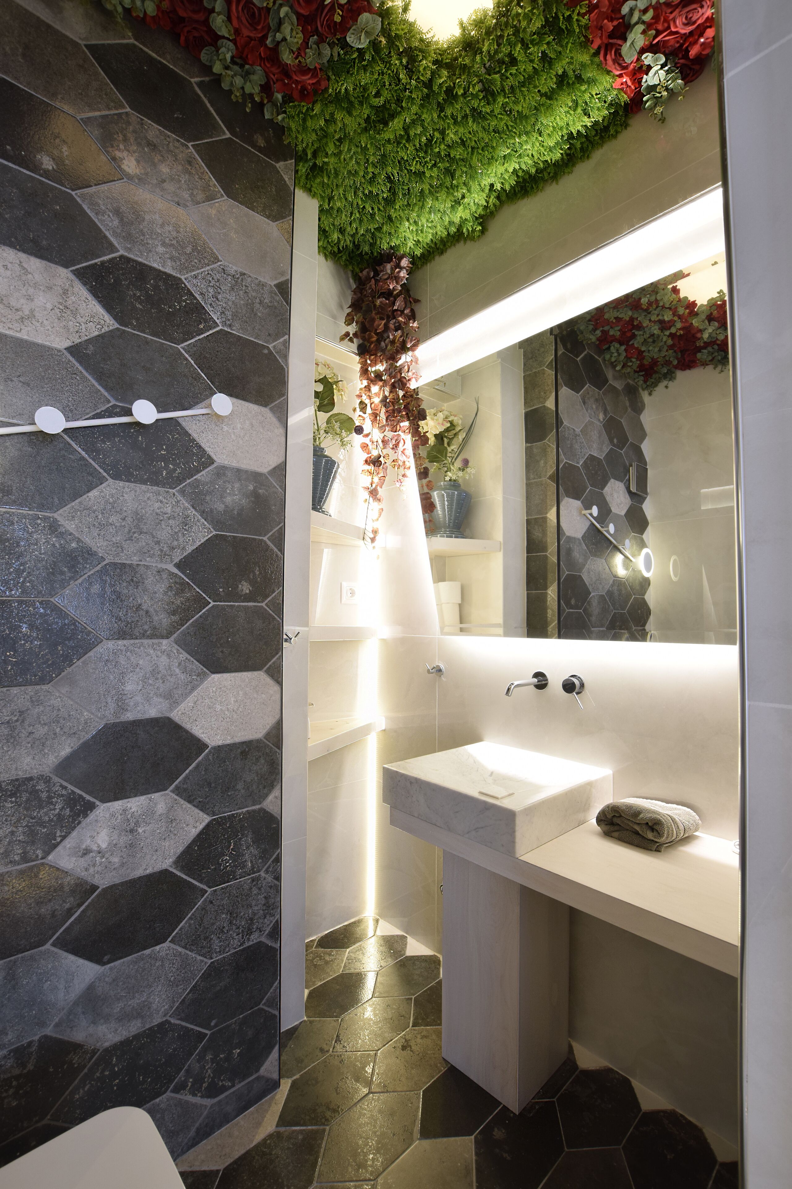A bathroom with a hexagonal tile floor, a white sink, and a mirror with a green plant hanging above.