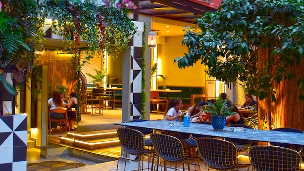 An outdoor dining area with a table and chairs, surrounded by greenery and a building with a colorful facade. - John's Hotel (Chalcis)