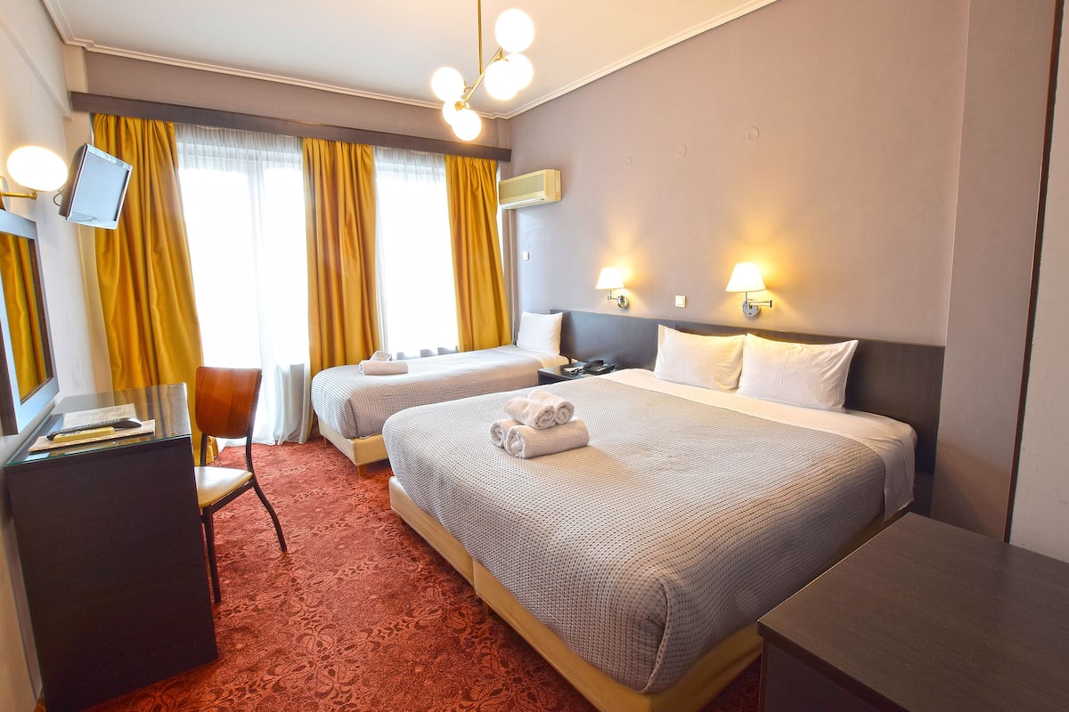A hotel room with two beds, a desk, a chair, and a TV.
