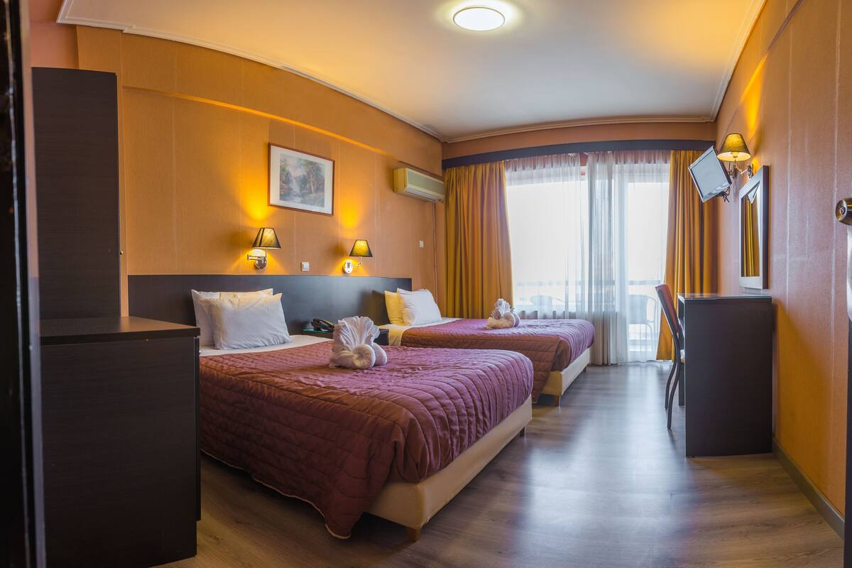 A hotel room with two beds, a desk, and a TV.