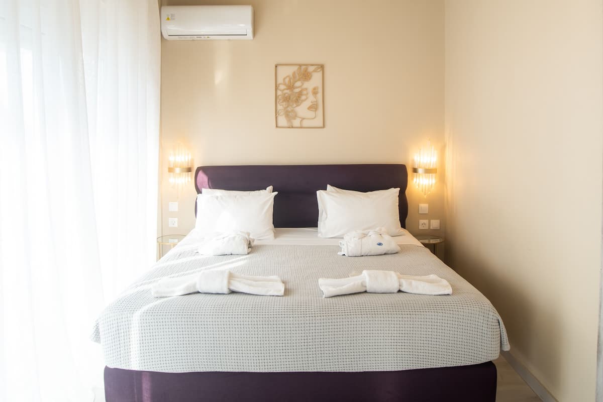 A neatly made bed with white linens, a purple headboard, and two bedside lamps.