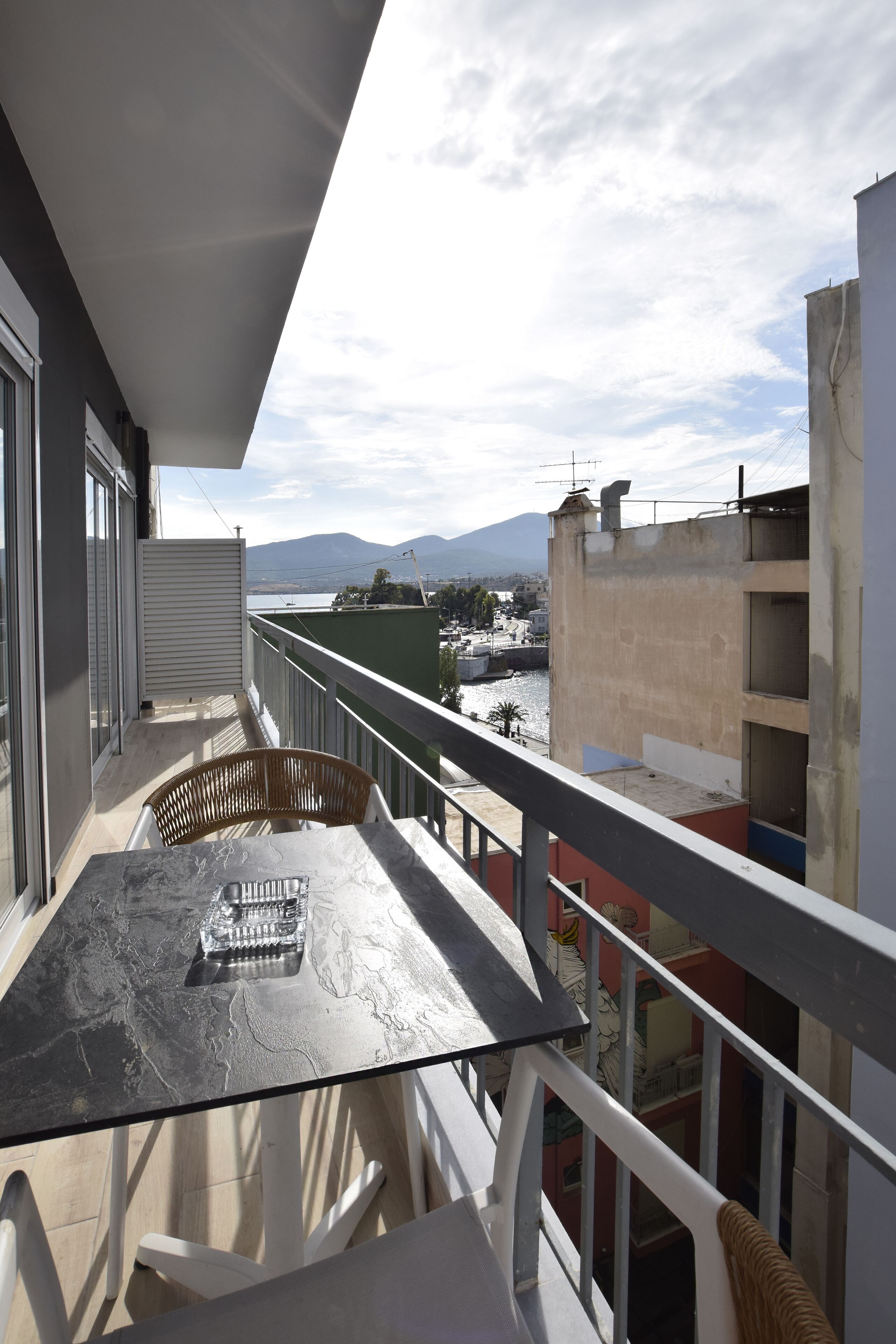 A balcony with a table and chairs, overlooking a body of water and buildings.