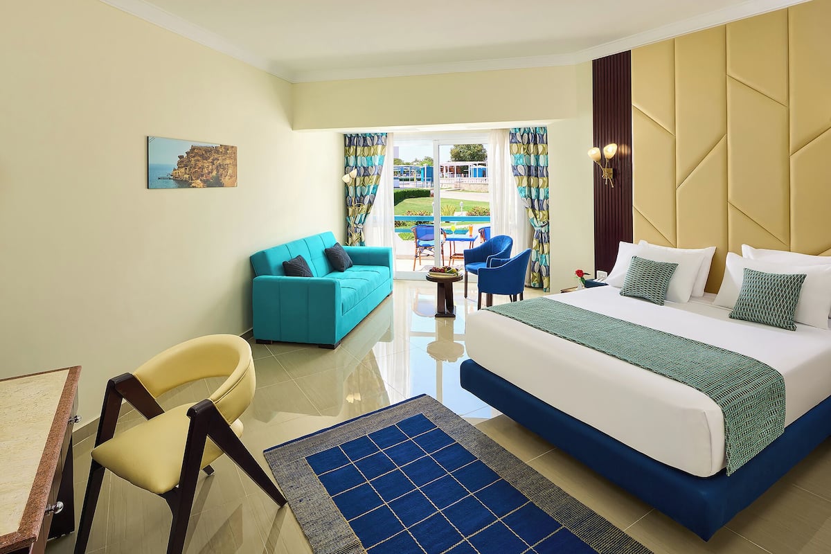 A hotel room with a bed, a sofa, a chair, a small table, and a view of the outdoors.