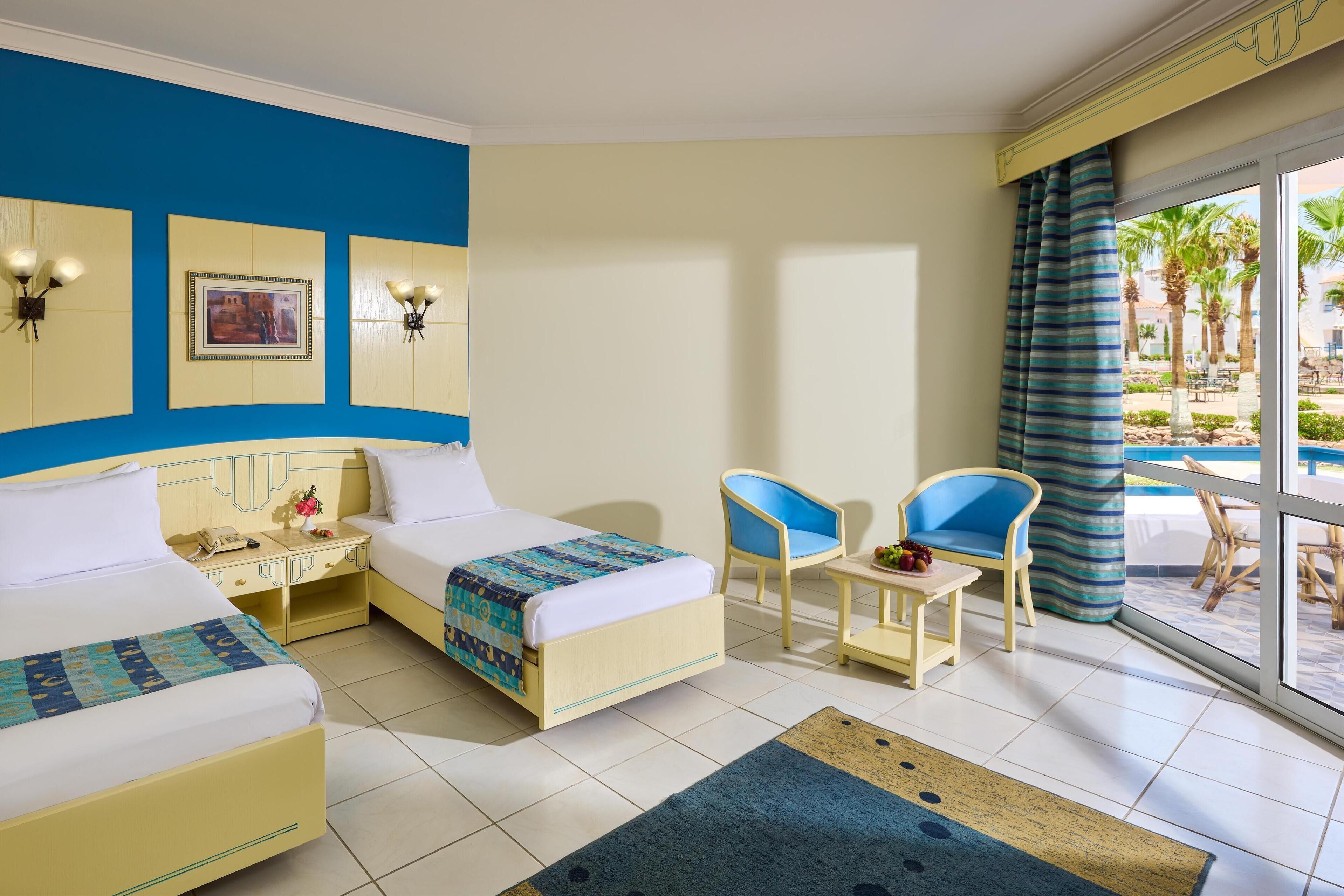 Habitación de hotel con dos camas, una mesita, dos sillas y vistas al área exterior.