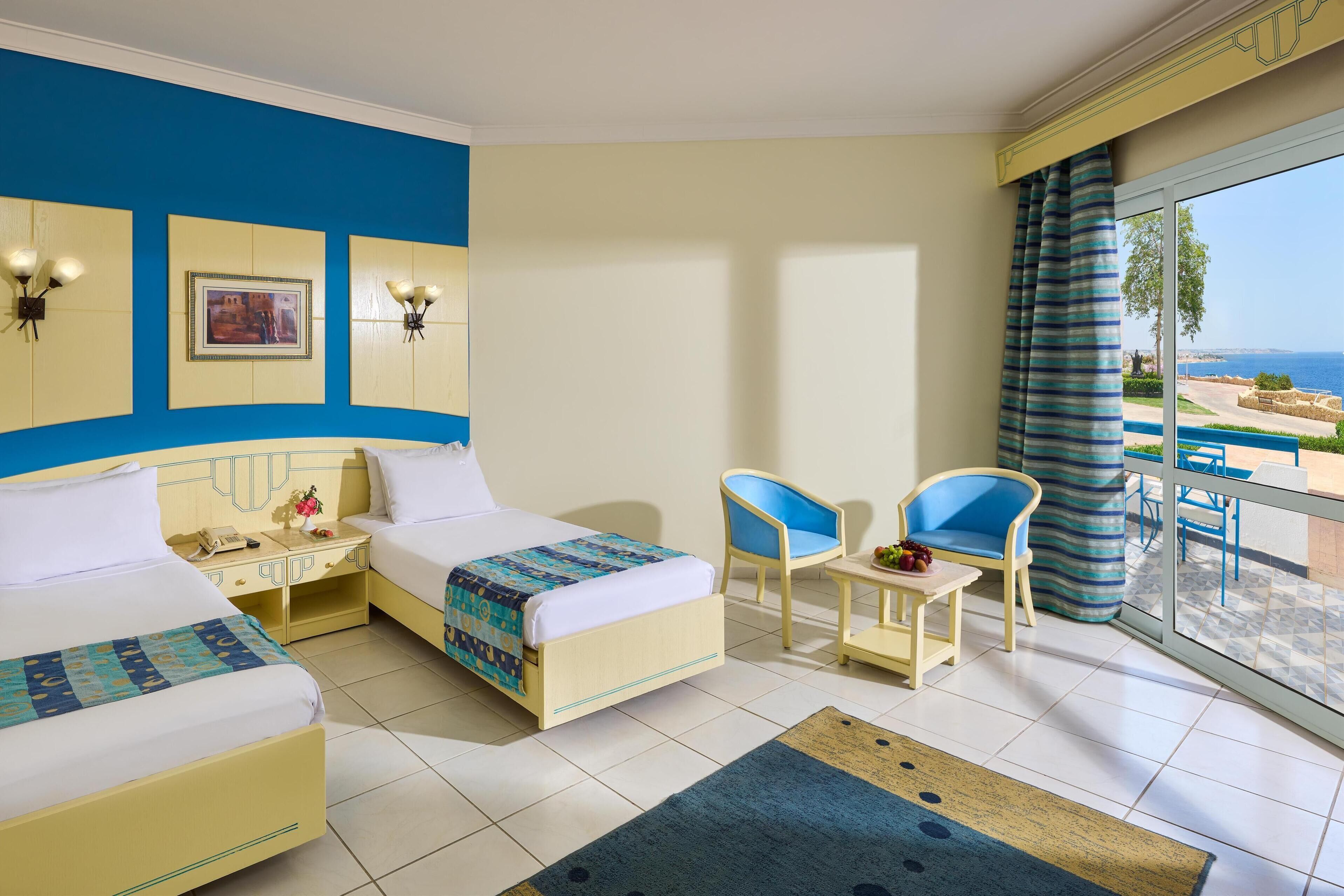 A hotel room with two beds, a balcony with a view, and a dining area.