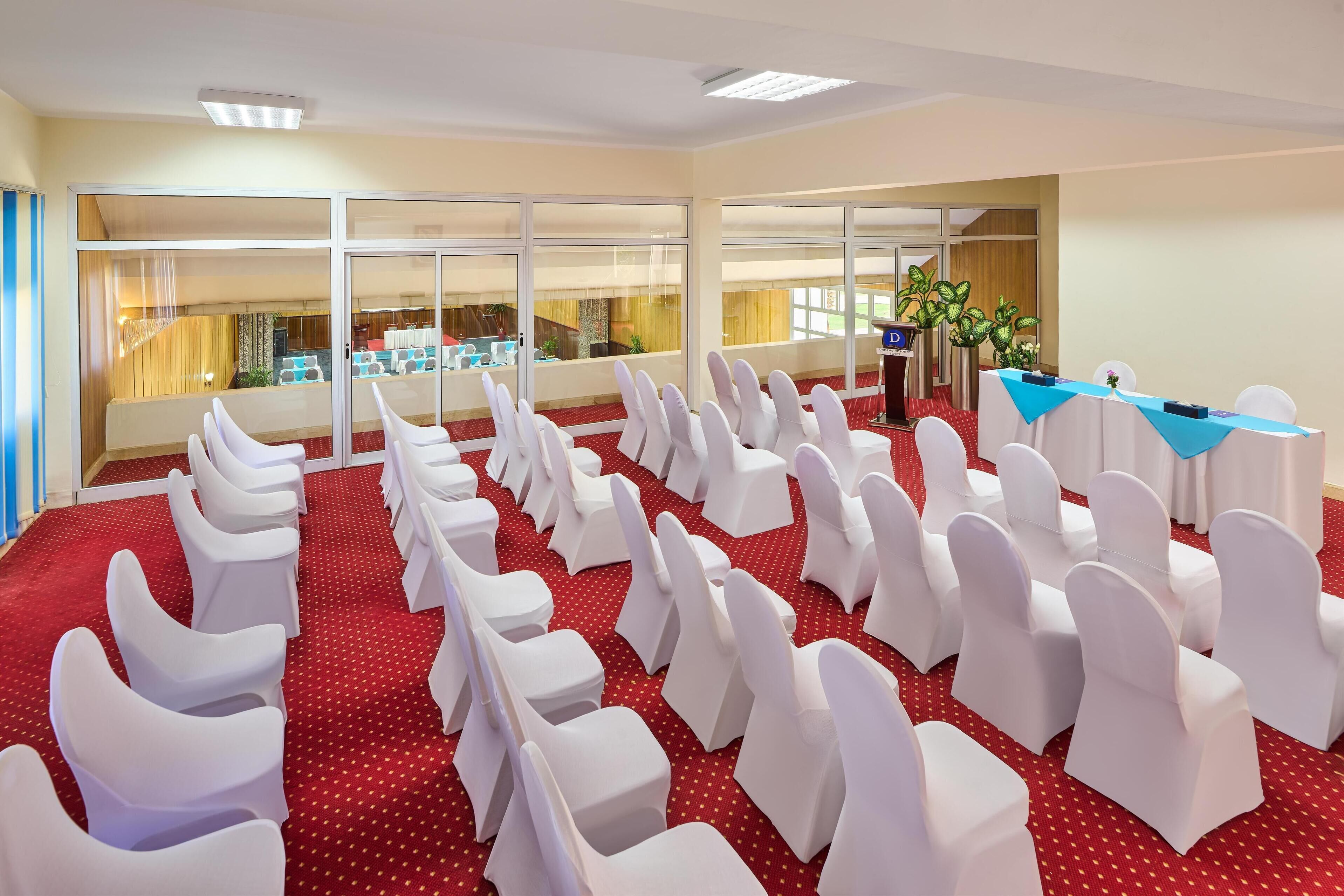 Uma sala de conferências com fileiras de cadeiras brancas, um púlpito e um balcão de recepção.