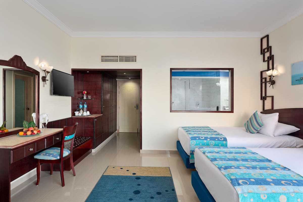 A hotel room with a desk, chair, two beds, a large mirror, and a window with a view.