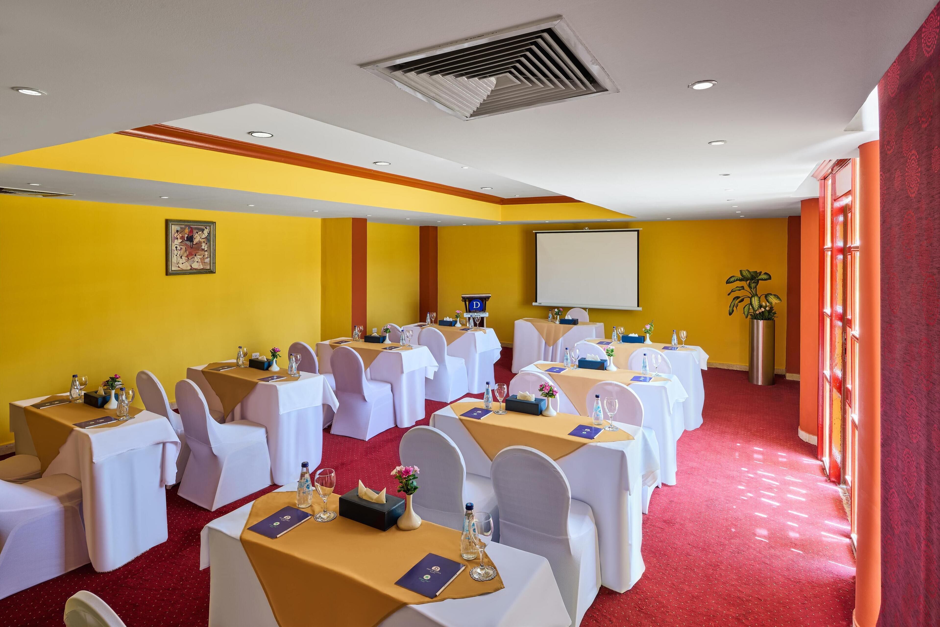 A conference room with multiple tables, white chairs, and a projector screen.