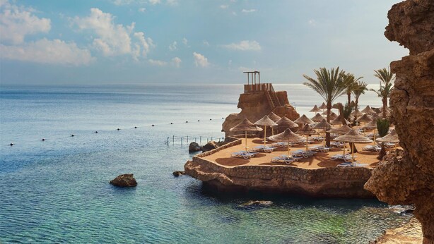 A beach resort with a rocky platform, palm trees, and thatched umbrellas. - Dreams Beach Sharm el Sheikh (Sharm El Sheikh)