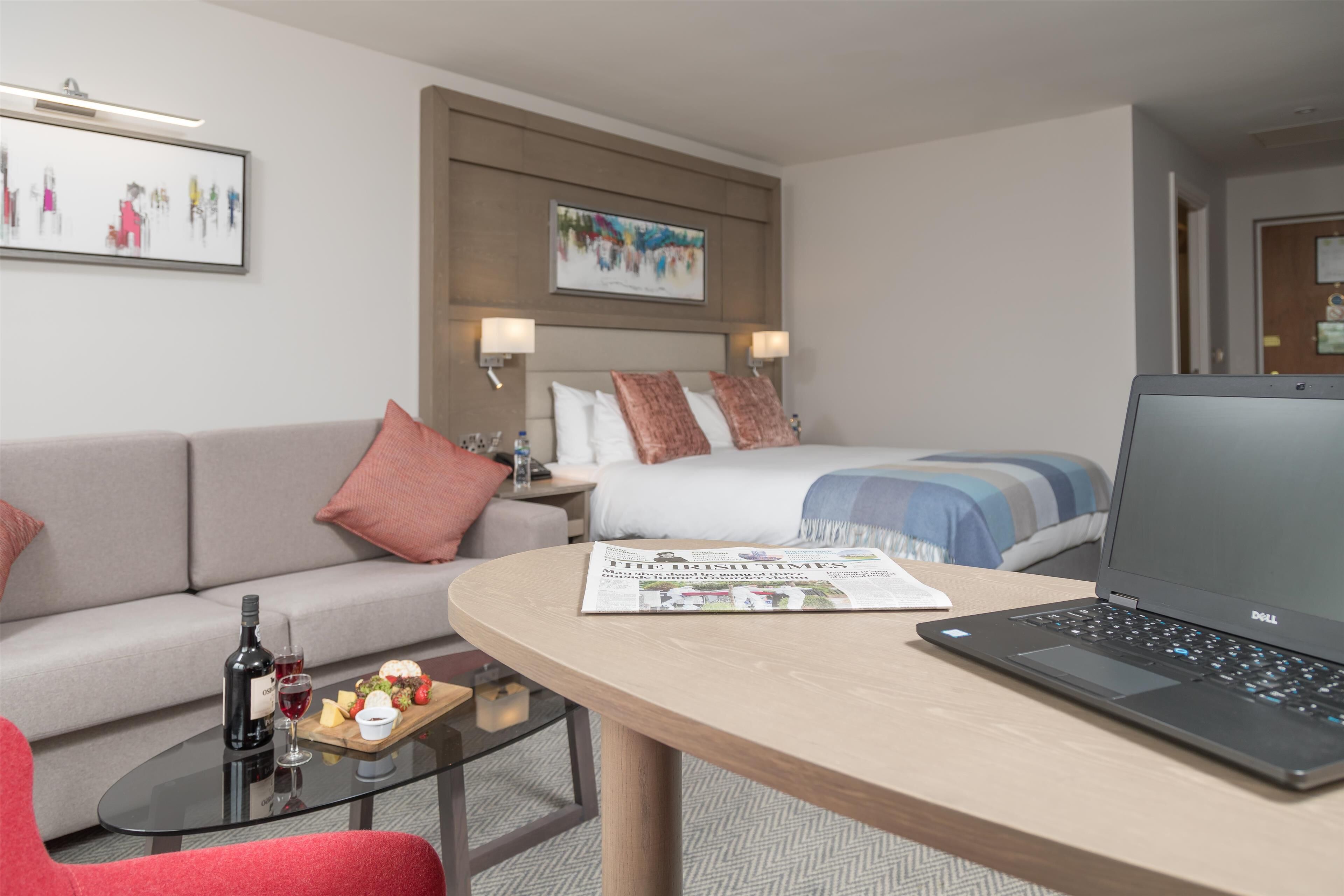 Una habitación de hotel con una cama, un sofá, una mesita de centro, una computadora portátil y un periódico.