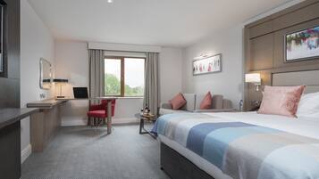 Ein modernes Hotelzimmer mit einem großen Bett, einem Schreibtisch mit einem Laptop, einem roten Sessel, einem kleinen Tisch mit einer Flasche und Gläsern sowie einem Fenster mit Vorhängen.